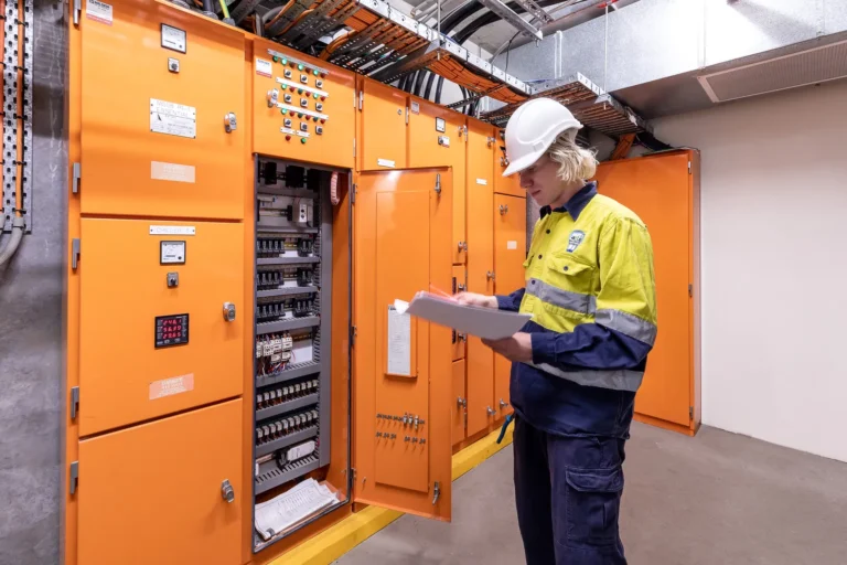 Worker inspecting electrical control panel in industrial setting.