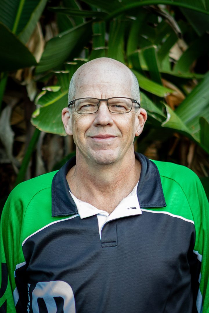 Man smiling in a work shirt near greenery.
